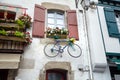 Bicycle is hanging under the window with wooden shutters on the wall of the facade of the building. Traditional red and white Royalty Free Stock Photo