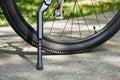 Bicycle kickstand with rear bicycle wheel standing on the asphalt with green grass on the background