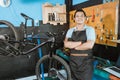 bicycle mechanic in smiling apron holding bicycle with crossed hands while standing beside bicycle