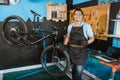 bicycle mechanic in smiling apron holding bicycle with thumbs up while standing beside bicycle