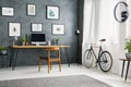 Bicycle next to wooden chair at desk in grey home office interior with posters. Real photo Royalty Free Stock Photo