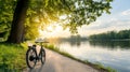 A bicycle parked on a path by a lake, sun setting in the background. Green trees line the path and the water\'s edge Royalty Free Stock Photo