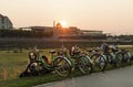 Bicycle rental on the river embankment at sunset. Many touring bicycles stand against the backdrop of the river and the old