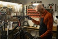 Bicycle repair in workshop. Old male mechanic working in bicycle repair shop, repairing bike in his garage Royalty Free Stock Photo