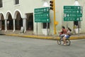 Bicyclist riding through town center of colonial village of Valladolid, in Yucatan Peninsula, Mexico with signs pointing to Merida
