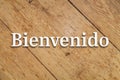 `Bienvenido` white text on a wooden background. Translation: `Welcome`