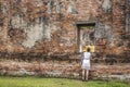 Big ancient old red brick wall where has a window frame can see thai ancient statues buddha while a female look through the window Royalty Free Stock Photo