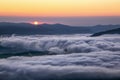 Big beautiful sun raises from the mountains and enlightens the sky with orange colour. Thick mysterious fog. Touristic place. Royalty Free Stock Photo