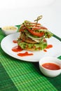 Big beef steak burger with vegetables and herbs on white plate on green bamboo placemat Royalty Free Stock Photo