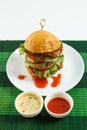 Big beef steak burger with vegetables and herbs on white plate on green bamboo placemat Royalty Free Stock Photo