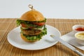 Big beef steak burger with vegetables and herbs on white plate and sauces on bamboo placemat Royalty Free Stock Photo