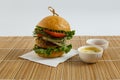 Big beef steak burger with vegetables and herbs on white plate and sauces on bamboo placemat Royalty Free Stock Photo