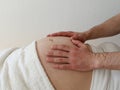 Big belly of a pregnant woman who lies in white clothes on her back. On the stomach are male hands. Close-up