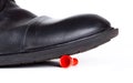 Big black boot crushing a small red game piece. Little object pinned down about to be destroyed under a large shoe, closeup Royalty Free Stock Photo