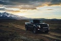 Big black matt American pickup truck Raptor rides on the Kurai steppe at sunset. Glaciers and Altai Mountains in the background.