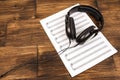 Big black professional headphones lying on the music sheet on the wooden background. Royalty Free Stock Photo