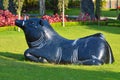 Big Black Wild Boar Statue In The Middle Of Wide Green Grass In Flower Garden Park