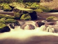 Big boulders covered by fresh green moss in foamy water of mountain river. Light blurred cold water with reflections, white