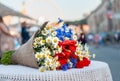 Big bouquet of wildflowers (camomile, knapweed, poppy) lays on the table with azure white tablecloth on blurry street