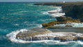 Big breaking ocean waves crash into the rocky cliffs and splash high into air