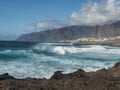 Big breaking waves splash against black lava rock coast. Turquoise blue Atlantic ocean with view of Los Gigantes cliffs Royalty Free Stock Photo