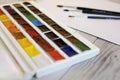 Watercolour paints palette, brushes and paper on wooden table. Close up view, selected focus. Working place of painter Royalty Free Stock Photo