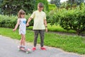 Big brother teaches little sister skateboarding in the park, holding her hand