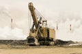 Big bucket mining excavator on a crawler track against a background of dense factory smog and fog with smoking chimneys. Heavy ind