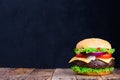 Big burger on wooden table with blank black chalkboard on background Royalty Free Stock Photo
