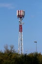 Big cell phone red and white antenna tower with multiple antennas and transmitters on top surrounded with street lights and tall