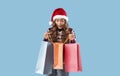 Big Christmas sale. Surprised young lady in Santa hat peeking into gift bags over blue background Royalty Free Stock Photo