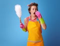 Modern housewife with duster brush sneezing on blue