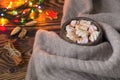 Big cup of hot cocoa with marshmallow, cinnamon and nurs and warm blanket on an old vintage wooden and Christmas light.