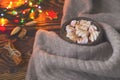 Big cup of hot cocoa with marshmallow, cinnamon and nurs and warm blanket on an old vintage wooden and Christmas light. Cozy chris