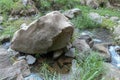 Big dark stone abstract shape on the river bank. A piece of rock supported by smaller stones in a shallow river. Stony riverbed. Royalty Free Stock Photo