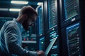 Big data Technician Works on Laptop next to a Server Cabinet in Big Data Center. He Runs Diagnostics and Maintenance, Sets System