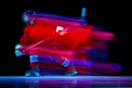 Dynamic portrait of energetic hockey player training with hockey stick isolated over dark background in mixed neon glow