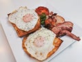 Big English breakfast with sunny fried eggs, bacon, tomatoes, ham on Turkish flat grilled bread on white dish