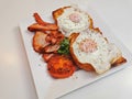 Big English breakfast with sunny fried eggs, bacon, tomatoes, ham on Turkish flat grilled bread on white dish