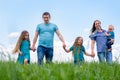 Big family dad, mom and three children walk on green grass against blue sky. Happy caucasian parents, two daughters and Royalty Free Stock Photo