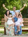 Big family sit on wooden bench in city park and waving, summer season, child, parent and grandmother, group of five people Royalty Free Stock Photo