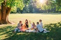 Big family sitting on picnic blanket in city park linden treeb during weekend Sunday sunny day. They are chatting and eating Royalty Free Stock Photo