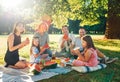 Big family sitting on the picnic blanket in city park during weekend Sunday sunny day. They are smiling, laughing and eating Royalty Free Stock Photo