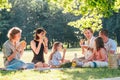 Big family sitting on the picnic blanket in city park during weekend Sunday sunny day. They are smiling, laughing and eating Royalty Free Stock Photo