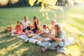 Big family sitting on the picnic blanket in city park during weekend Sunday sunny day. They are smiling, laughing and eating Royalty Free Stock Photo