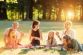 Big family sitting on the picnic blanket in city park during weekend Sunday sunny day. They are smiling, laughing and eating Royalty Free Stock Photo