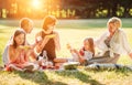 Big family sitting on the picnic blanket in city park during weekend Sunday sunny day. They are smiling, laughing and eating Royalty Free Stock Photo