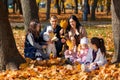 a big family sitting together in a glade of yellow maple leaves in an autumn city park, children and parents, happy people Royalty Free Stock Photo