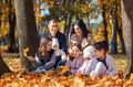 a big family sitting together in a glade of yellow maple leaves in an autumn city park, children and parents, happy people Royalty Free Stock Photo