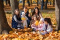 a big family sitting together in a glade of yellow maple leaves in an autumn city park, children and parents, happy people Royalty Free Stock Photo